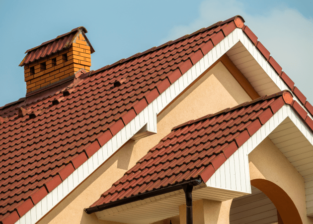 Roof with red tiles and chimney, showcasing architectural details and clean lines against a blue sky.